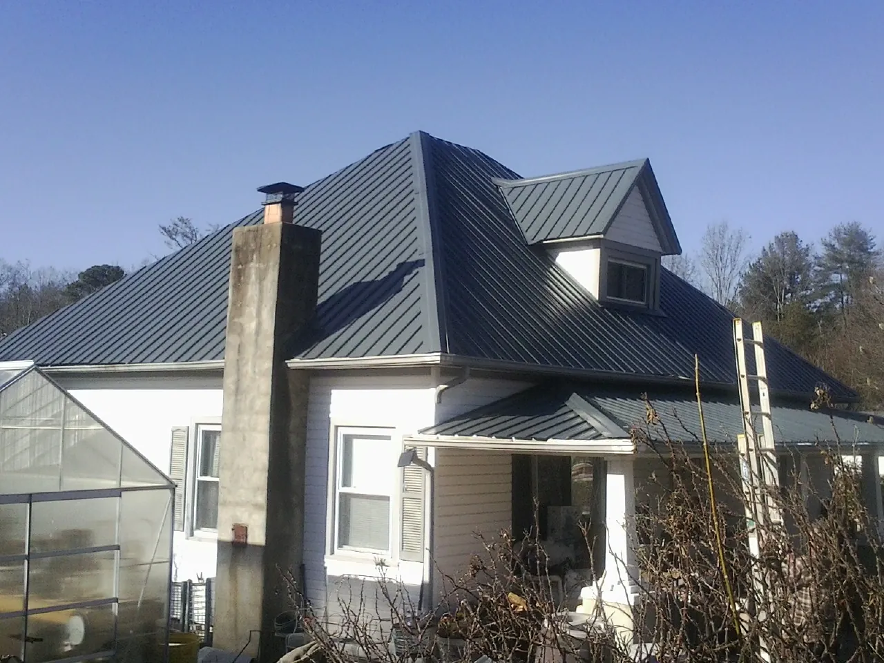 Dark blue standing seam metal roof on a white farmhouse with dormer — Slate & Tile Roof Repair by Roofing Brothers in Pleasant Hill