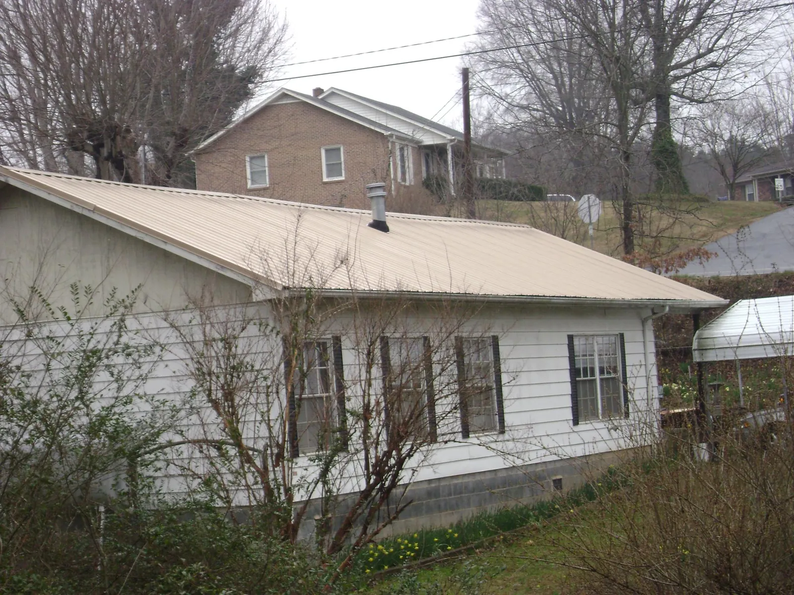 Tan metal roof on a white sided house set into a hillside — Commercial Roofing by Roofing Brothers in Pleasant Hill